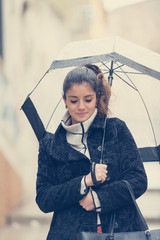 Dark-haired young woman walks through the streets of Caceres with a transparent umbrella on a rainy day