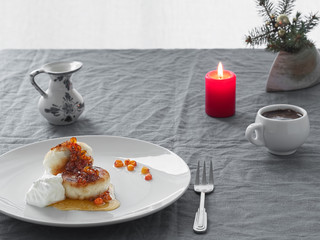 Cheesecakes or curd pancakes with cream and sea buckthorn jam on a white plate, on a gray tablecloth. Vintage gravy boat, espresso. Homemade сottage cheese fritters. Tasty breakfast. Closeup.