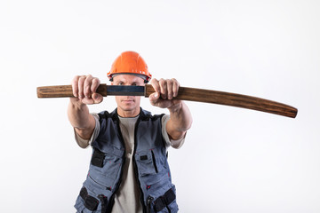 The builder pulls a katana from its sheath, in front of him. Repairman wearing a helmet and work clothes.