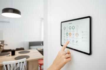 Controlling home with a digital touch screen panel installed on the wall. Close-up on a screen with mobile application for managing smart devices