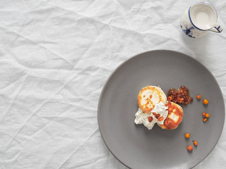 Cheesecakes or curd pancakes with cream and sea buckthorn jam on a gray plate, on a white tablecloth. Vintage gravy boat. Homemade сottage cheese fritters. Tasty breakfast. Top view. Copy space.