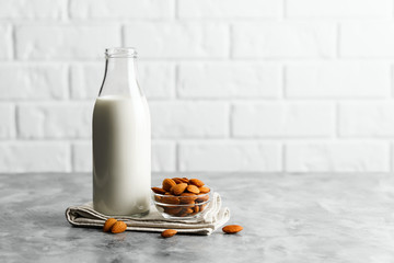 Glass reusable bottle with almond milk and almonds on a marble countertop, kitchen with a white brick wall.