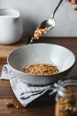 Hand sprinkles baked granola in a ceramic bowl. Healthy vegetarian breakfast.