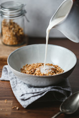 Almond milk is poured in a ceramic bowl with baked granola. Healthy vegetarian breakfast.