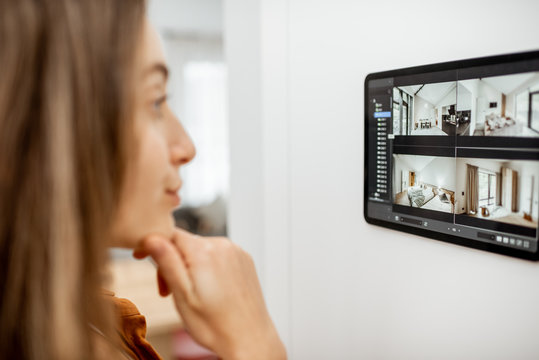 Young woman watching video from security cameras on a digital tablet at home. Concept of remote video surveillance over the internet with smart devices