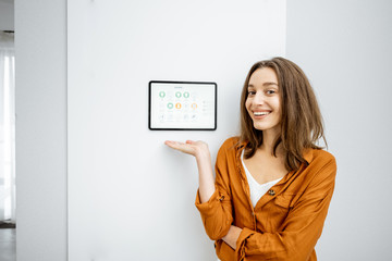 Portrait of a young and happy woman standing near touch screen panel for smart home control in the...