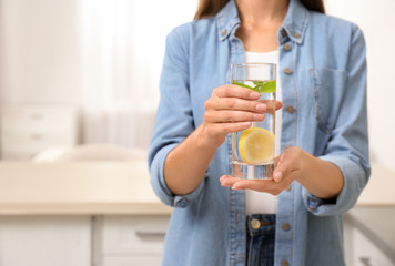 Young woman with glass of lemon water at home, closeup. Space for text