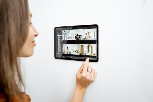 Young woman watching video from security cameras on a digital tablet at home. Concept of remote video surveillance over the internet with smart devices