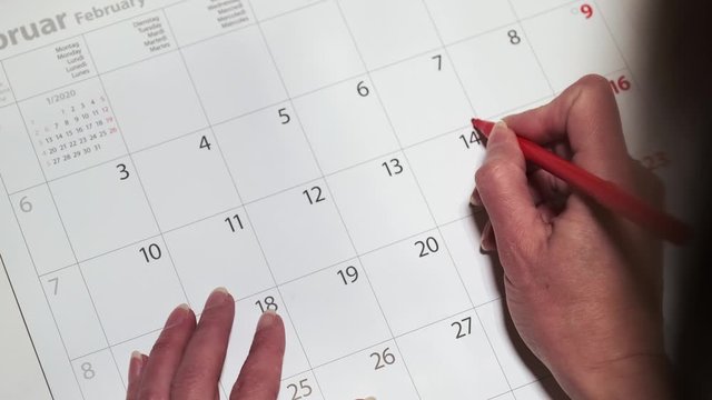 Woman draws a heart on a calendar February 14 in bright colors. Valentine's day reminder concept.