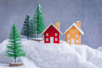 Miniature wooden houses village on the snow over blurred Christmas decoration background, toned