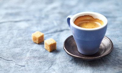 Cup of coffee and two brown sugar cubes on bright background. Close up.