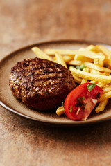 Fried hamburger steak with tomatoes and french fries. Rustic background. Close up. 