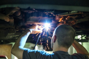 auto mechanic welds a part in a car on a lift