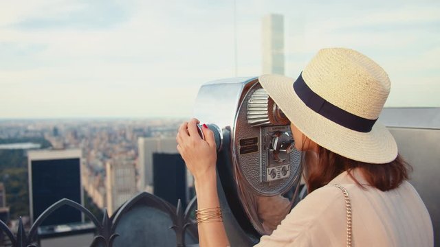 Young woman looking through binoculars at the viewpoint 