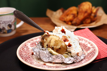 gebackene kartoffel mit knoblauchcreme und hähnchenschenkeln im hintergrund