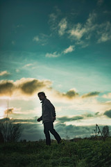 Fototapeta premium Mysterious man in rural landscape with cloudy sky at sunset.
