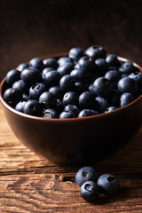 Fresh ripe blueberries in brown ceramic bowl on wooden table with dark background, ingredients for healthy diet lifestyle concept, dark and moody, 45 degree angle view, vertical format