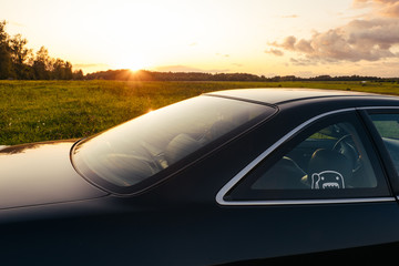 Fototapeta na wymiar Black coupe car in green field sunset time
