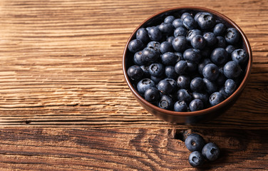 Fresh ripe blueberries in brown ceramic bowl on wooden background, ingredients for healthy diet lifestyle concept, 45 degree angle view, landscape horizontal format, copy space