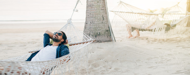 Naklejka premium A man enjoys calm, lies in a hammock on the background of the ocean and sunset.