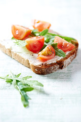 Tomato sandwich with cream cheese and fresh rocket on bright wooden background. Close up.