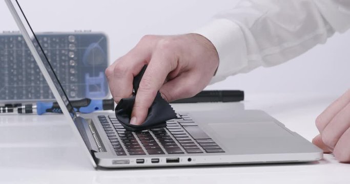 Service worker cleaning laptop keyboard buttons with microfibre cloth in white walled lab in 4k