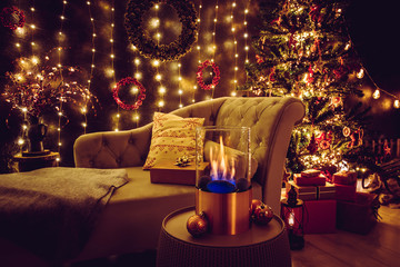 Selective focus on modern freestanding portable glass and copper metal fireplace burning bio ethanol gas on living room table with cozy Christmas eve home decor interior on background.