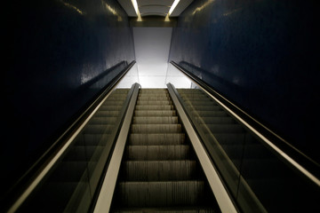 Escalator with recessed footlights glowing in darkness. Abstract transportation and architecture photo. Public interior of modern building, subway or railway station. Moving staircase in backlight.