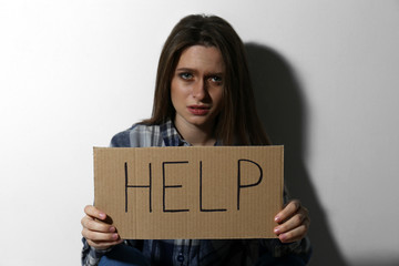 Abused young woman with sign HELP near white wall. Domestic violence concept