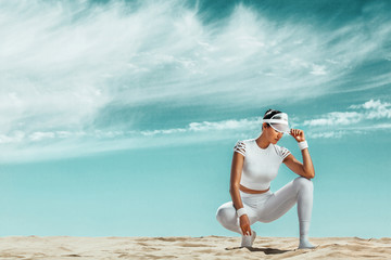 Sporty and fit young woman athlete relaxed after training at the desert. Cloudy day on coast. The concept of a healthy lifestyle and sport. Woman in white sportswear.