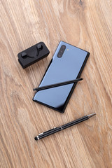 Smartphone with three cameras, stylus, pen and headphones on a wooden table close-up.