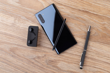 Smartphone with three cameras, stylus, pen and headphones on a wooden table close-up.