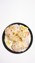 Two fresh chicken legs with spices and lemon in a black pan prepared for frying. Isolated on a white background. Asian and European cuisine.