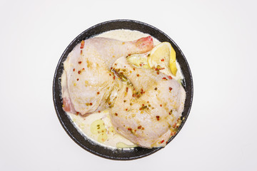 Two fresh chicken legs with spices and lemon in a black pan prepared for frying. Isolated on a white background. Asian and European cuisine.
