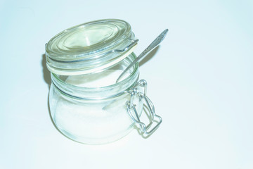 Glass transparent jar with sugar and a teaspoon inside. Top view on a white background with copy space.
