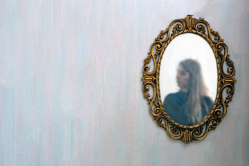 The reflection of a woman in a antique golden mirror in the vintage interior, old pattern wallpaper...