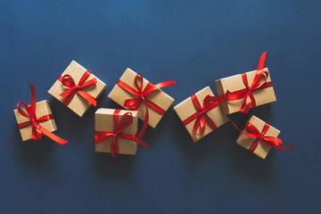 Christmas flat lay. Holiday gifts in boxes in craft paper and a red ribbon on a classic blue...