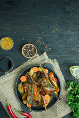Baked quail with vegetables in a pan. Space for text. Dark background.