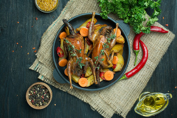 Baked quail with vegetables in a pan. Space for text. Dark background.