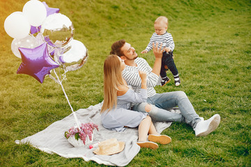 A young and beautiful blonde mother in a blue dress, along with her handsome man dressed in a white...