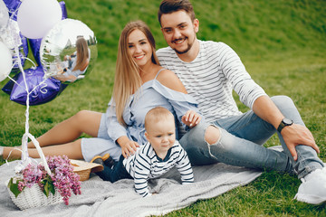 A young and beautiful blonde mother in a blue dress, along with her handsome man dressed in a white...