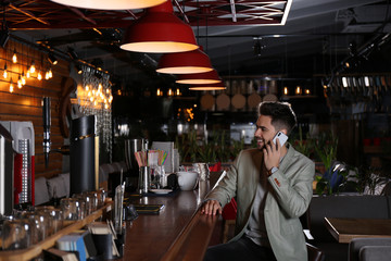 Young business owner talking on phone in his cafe