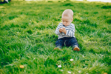 little cute handsome boy sits on a green grass in a sunny summer park