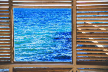 Square window overlooking the classic blue sea and blue sky. Wooden frame.