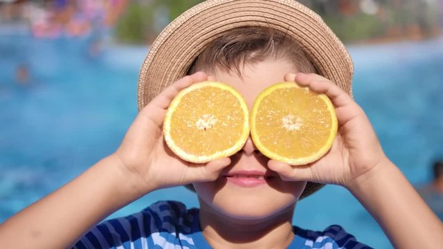 Close-up carefree travel cute boy posing with half of orange on eyes at sea beach background