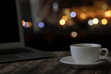 overtime in the evening, work from home, a cup of coffee and a laptop on a night background with beautiful bokeh