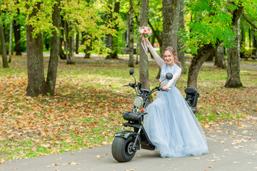 The bride in a wedding dress on a motorcycle with bouquets on the day of the wedding walk in the...