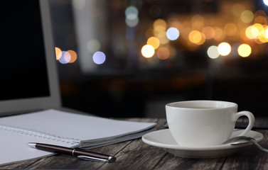 Obraz premium overtime in the evening, work from home, a cup of coffee and a laptop on a night background with beautiful bokeh