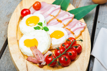 Tasty fried eggs with vegetables on a wooden plate.