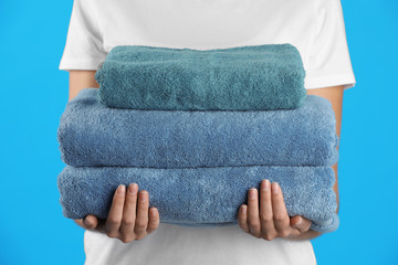 Woman holding fresh towels on light blue background, closeup